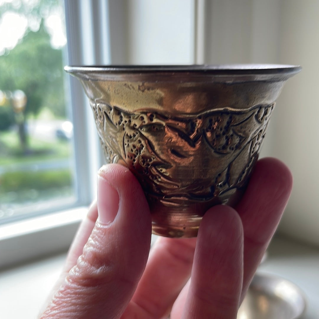 Close up image of a hand hooding a small metal cup with engraving from The Roving Root.